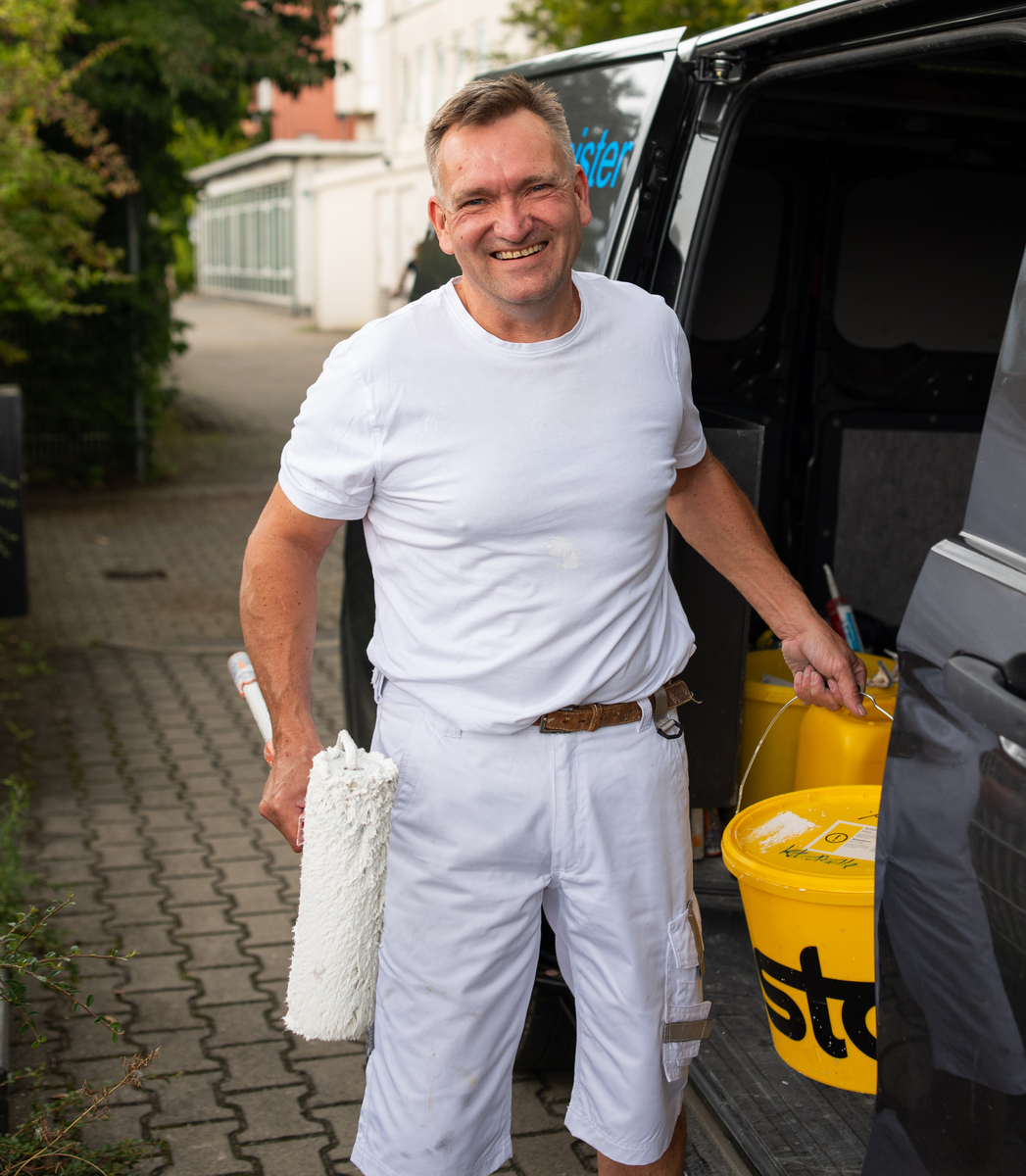 Malermeister Andreas Baßner steigt mit Farbrolle und Farbeimer aus seinem Auto – bereit für den Einsatz in Regensburg